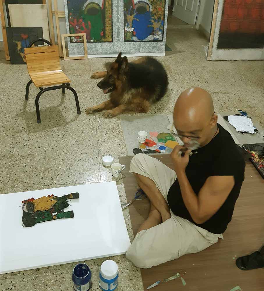 Basuki works on a new painting in his studio, alongside his dog